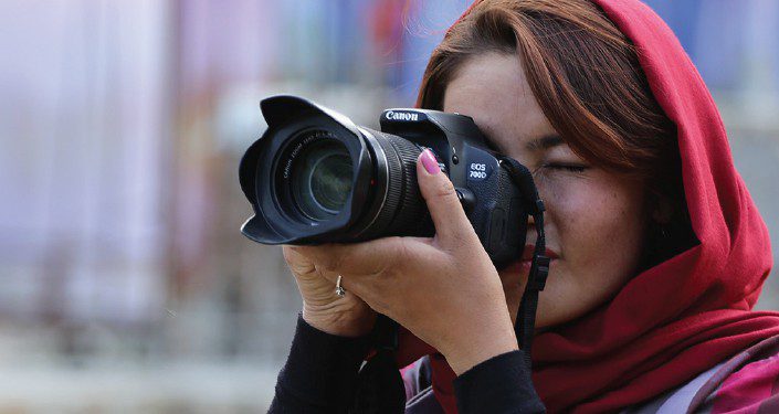 A woman wearing a scarf looks through the sight of a camera