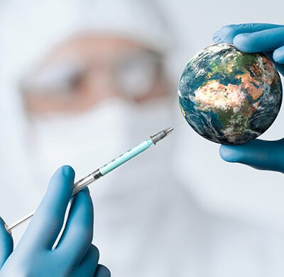 A person in PPE sticks a syringe into a ball made to look like planet earth.