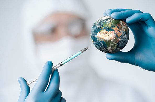 A person in PPE sticks a syringe into a ball made to look like planet earth.
