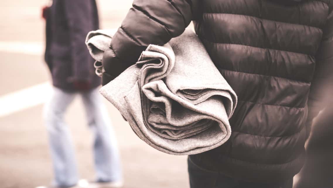 A person wearing a down jacket holds a blanket under their arm.