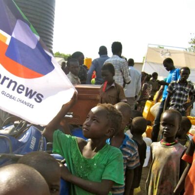 Children gather around a motor bike with speakers in a refugee camp.