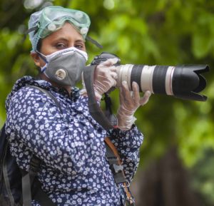 A woman wearing PPE holds a camera.
