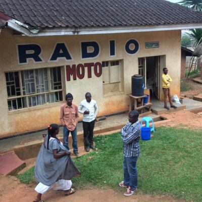Four people stand in front of a small concrete building with a sign "Radio Moto"