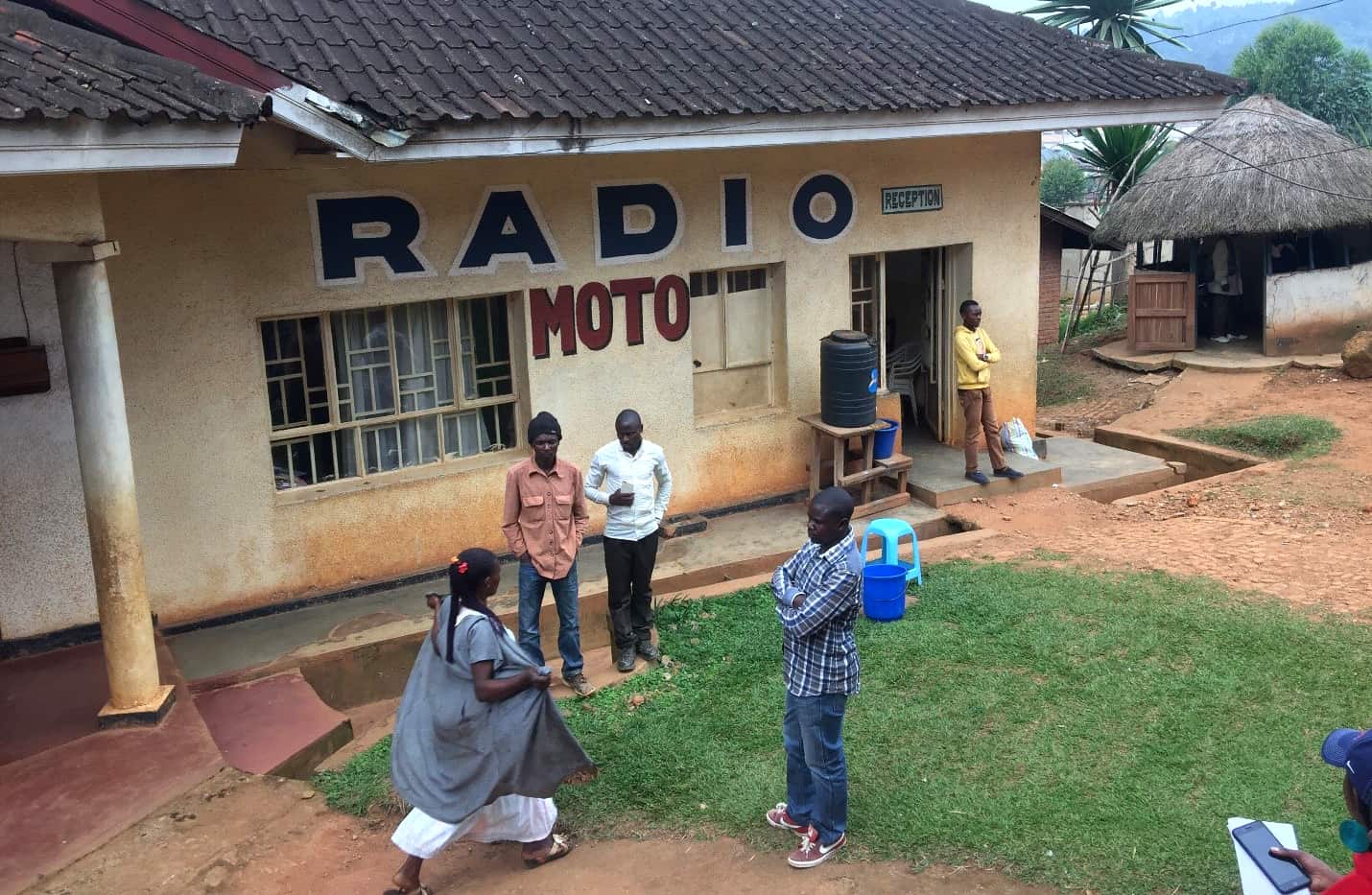 Four people stand in front of a small concrete building with a sign "Radio Moto"