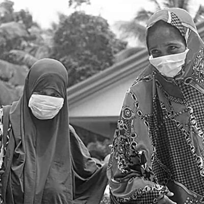 Two women wearing face masks stand outside a house.