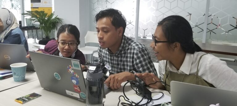 Two women and a man look at a laptop computer