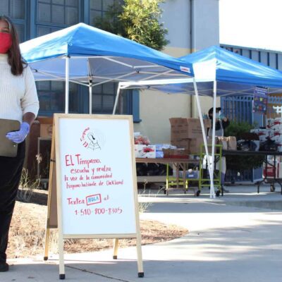 A woman stands outside a tent next to a white board advertising El Timpano