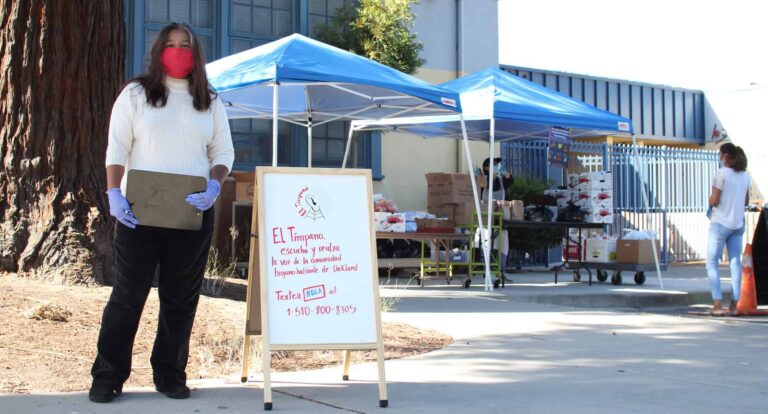 A woman stands outside a tent next to a white board advertising El Timpano