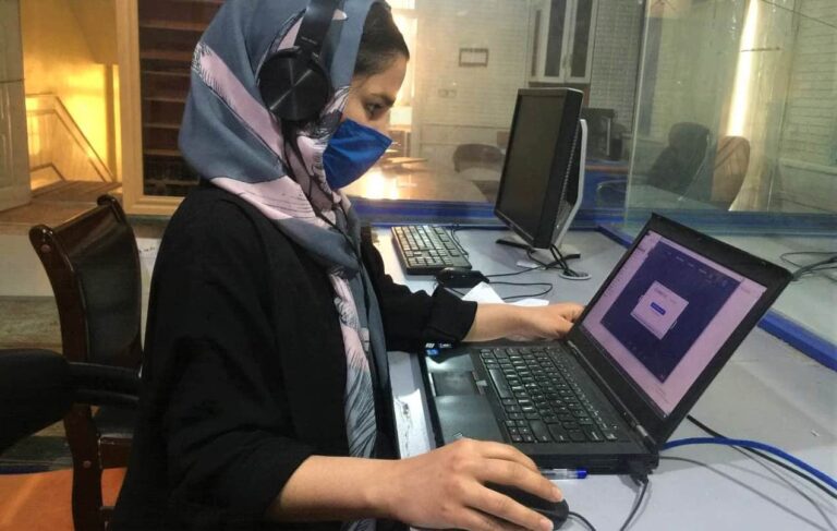 A woman wearing a face mask and a head scarf works on a laptop computer