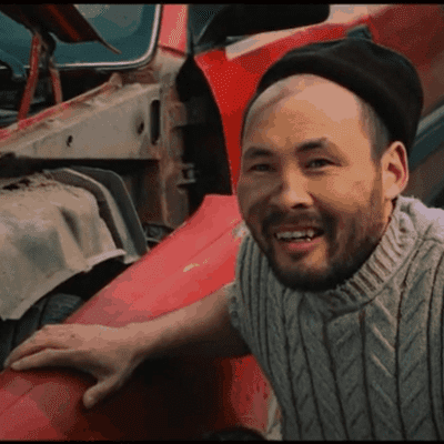 A bearded man wearing a hat puts his hand on the side of a red truck