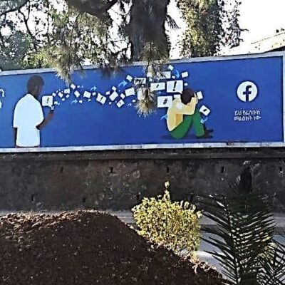 A billboard with Amharic script and a Facebook logo along side of a road.