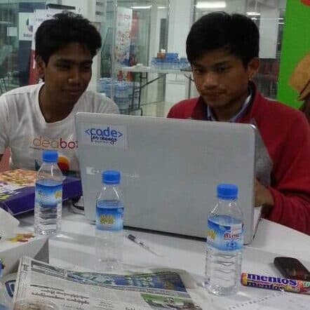 Two young men work together on a computer at a hackathon in Myanmar