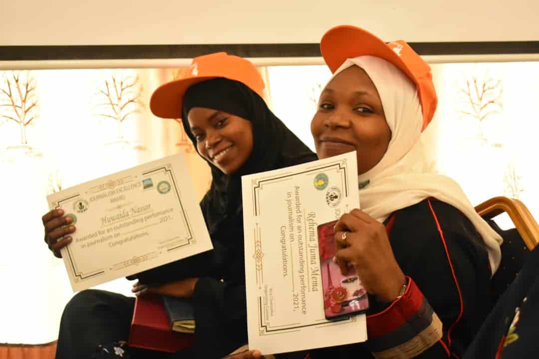 Two women, both wearing orange caps, hold certificates in their hands.