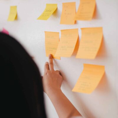 A woman stands next to a board with post-its on it.