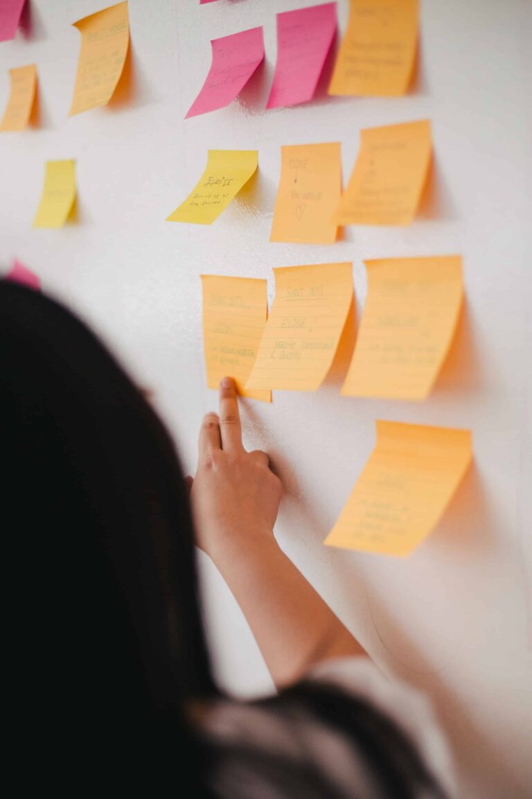 A woman stands next to a board with post-its on it.