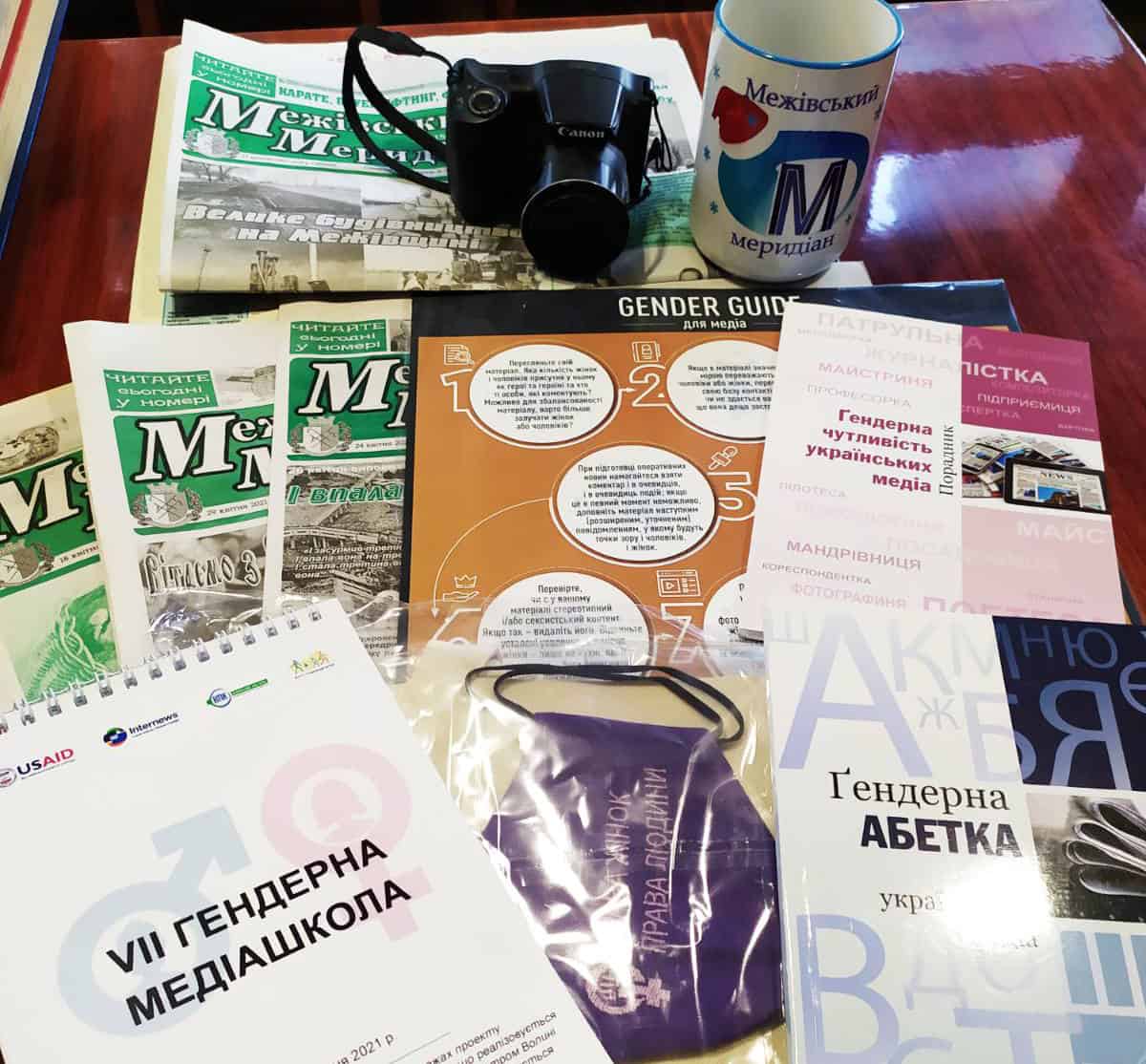 A camera and a mug sit on some newsletters and pamphlets