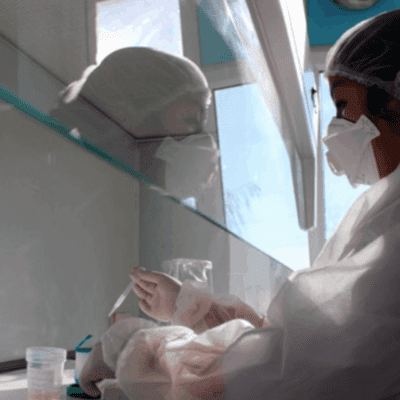A woman wearing PPE works in a lab.