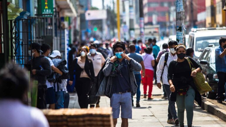 People walk down the sidewalk in a city - most are wearing face masks.