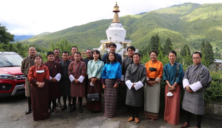 A group of people stand together posing with a temple and green hills behind them.