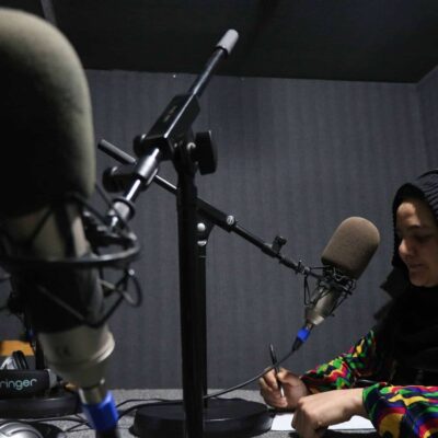 A woman sits at a microphone in a radio studio.