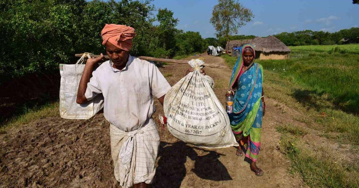 Two people carry bundles down a dirt path.