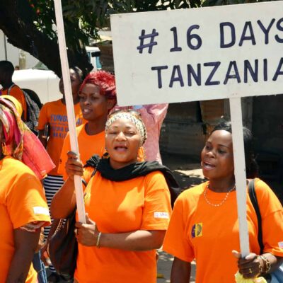 Women wear orange t shirts and hold protest signs: "#16 days # Tanzania"