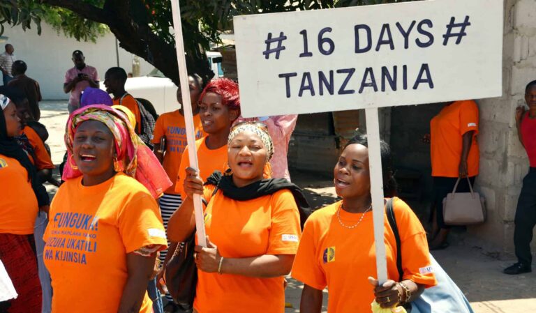 Women wear orange t shirts and hold protest signs: "#16 days # Tanzania"