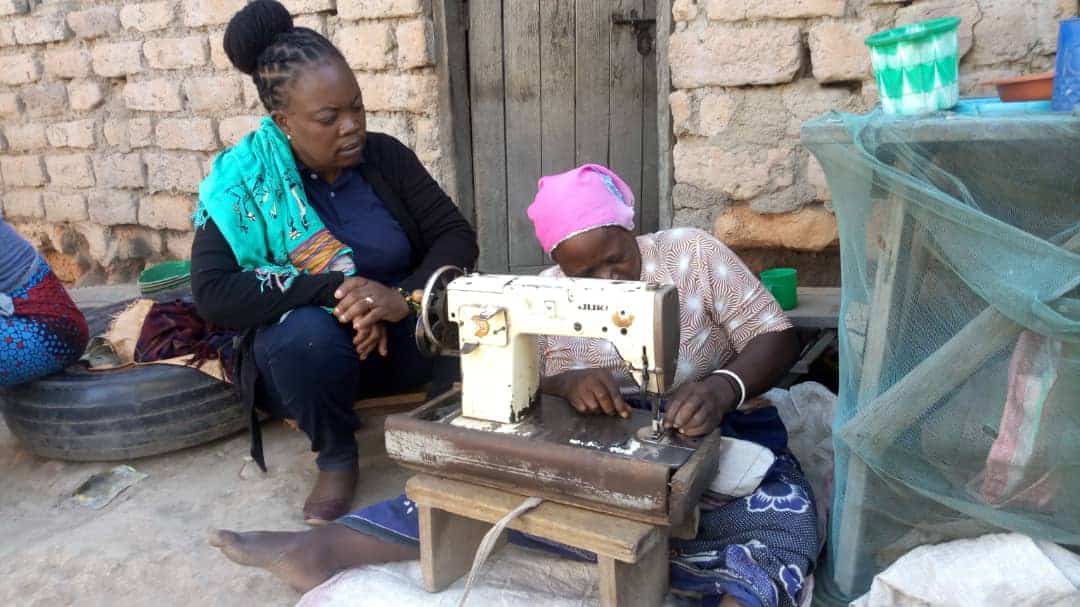 A woman watches another woman working on sewing machine..