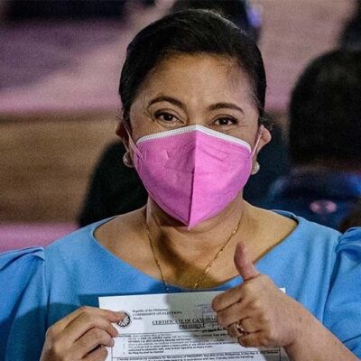 A woman wearing a face mask gives a thumbs up.