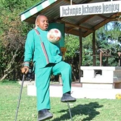 A man using crutches kicks a soccer ball.