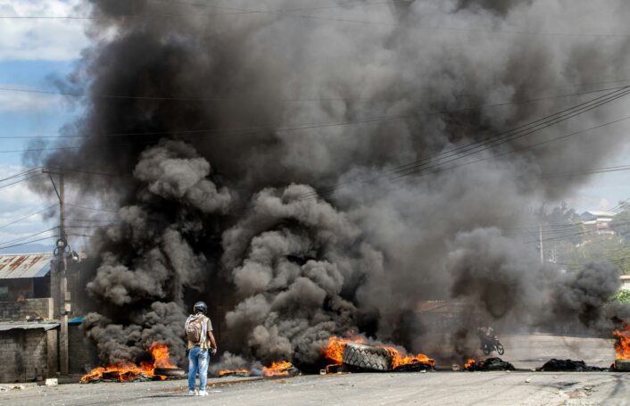 Reporter captures video in front of burning barricade in Haiti during protest.