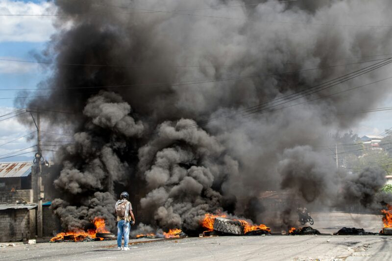 Reporter captures video in front of burning barricade in Haiti during protest.